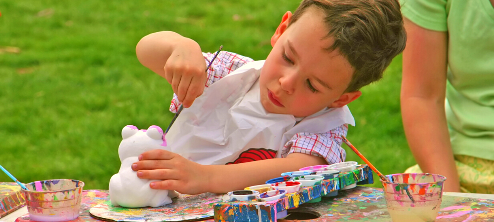 A young boy painting a plaster frog outside