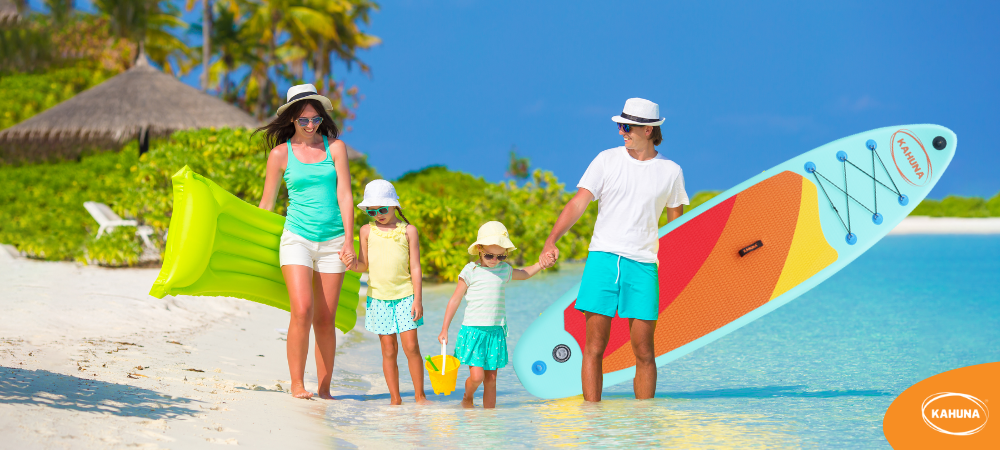 A dad carrying a paddle board at the beach with his family