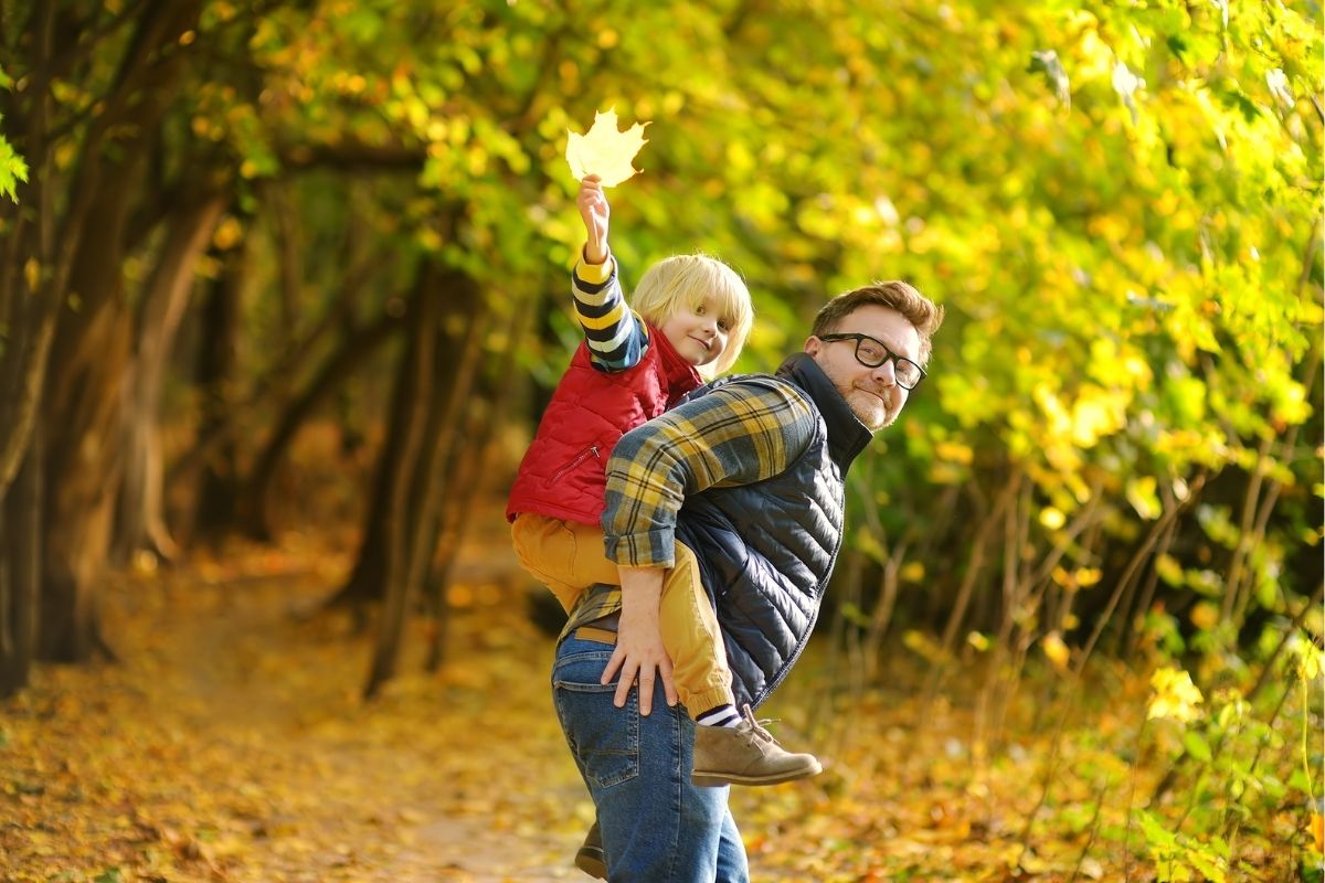 Toddler piggybacking on his dad while on an autumn hike